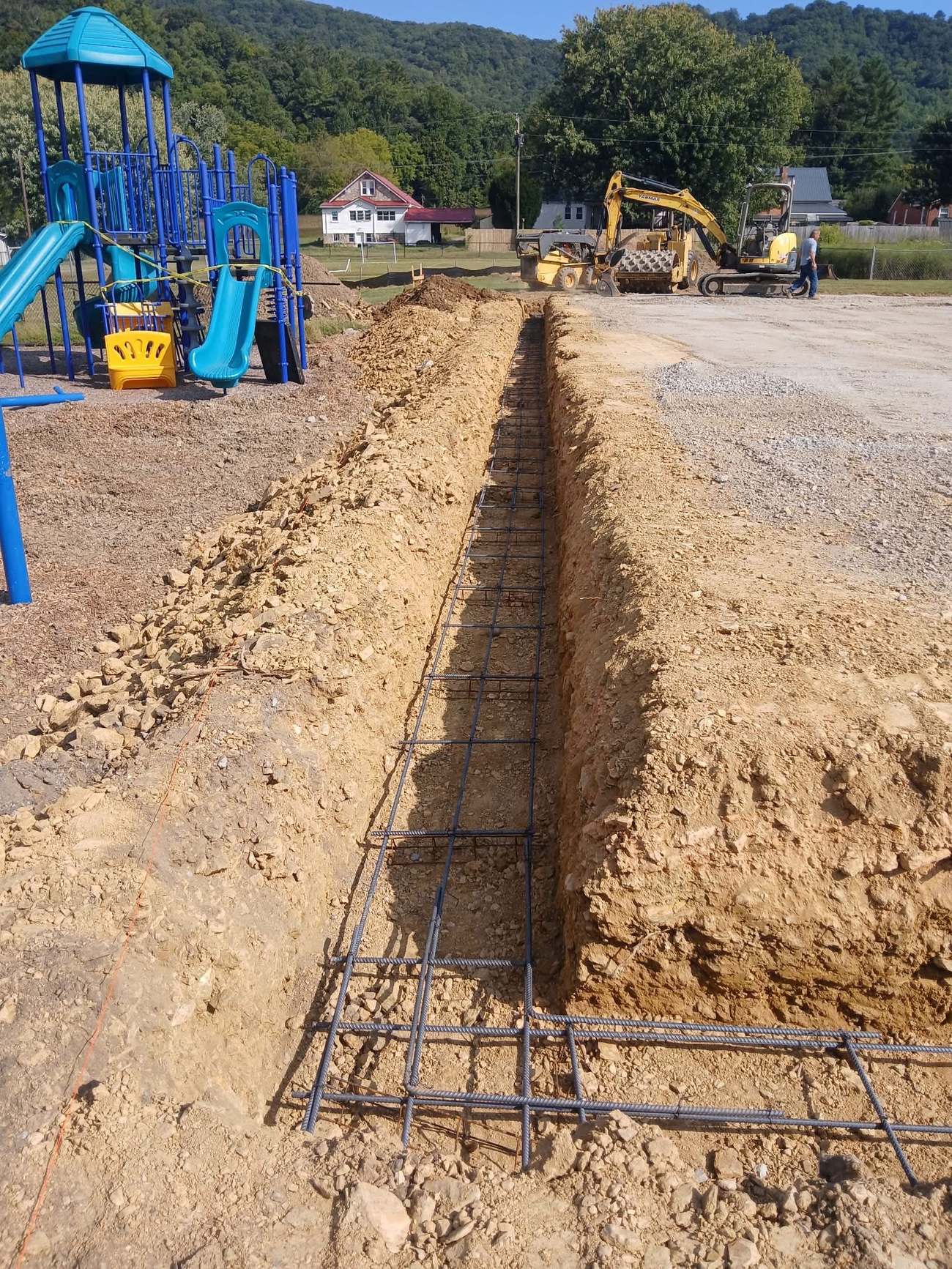Rebar-reinforced forms being prepared for a concrete pour near a public playground